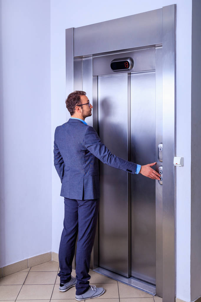 Νέος μοντέρνος επαγγελματίας με κοστούμι περιμένει μπροστά από το ασανσέρ - Φωτογραφία, εικόνα
