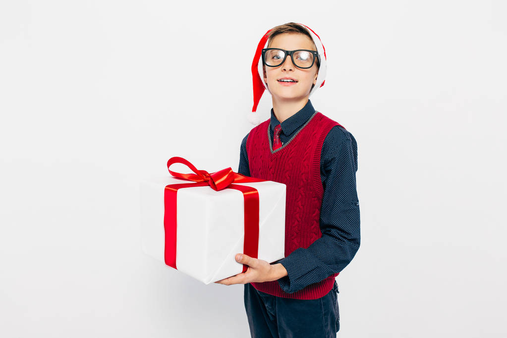 lustiger kleiner Junge mit roter Weihnachtsmütze. stilvoller Junge mit Weihnachtsgeschenk, auf weißem Hintergrund. - Foto, Bild