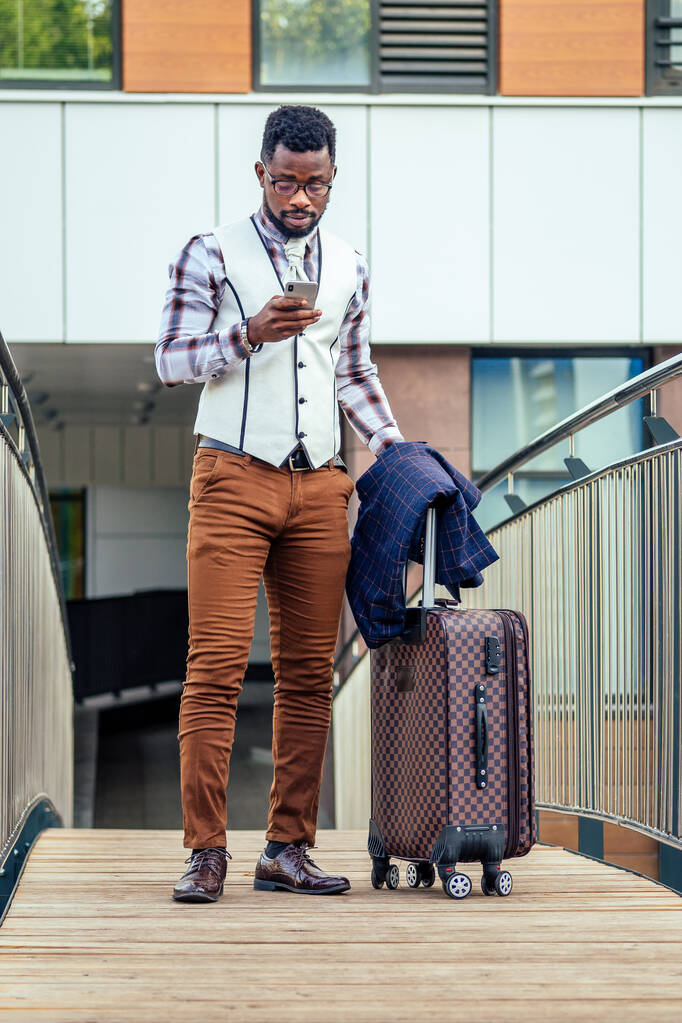Pełna długość portret udanego i dobrze ubranego afrykańskiego biznesmena amerykańskiego spaceru na lot na lotnisku z torbą na kółkach duża walizka na kółkach - Zdjęcie, obraz