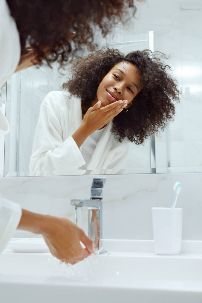Ihonhoito. Nainen pesee kasvot vedellä pesualtaassa kylpyhuoneessa
 - Valokuva, kuva