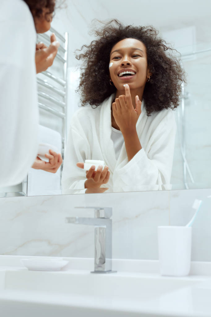 Hautpflege. Frau, die Gesichtscreme aufträgt, schaut in Badezimmerspiegel - Foto, Bild