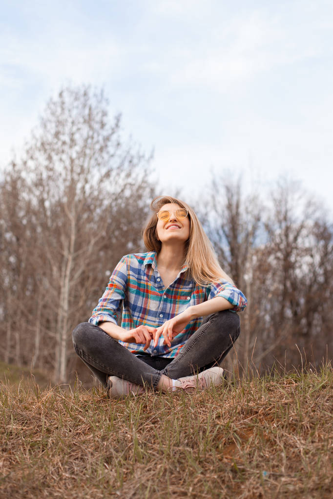 Ευτυχισμένη νεαρή γυναίκα που κάθεται στο λόφο το φθινόπωρο. - Φωτογραφία, εικόνα
