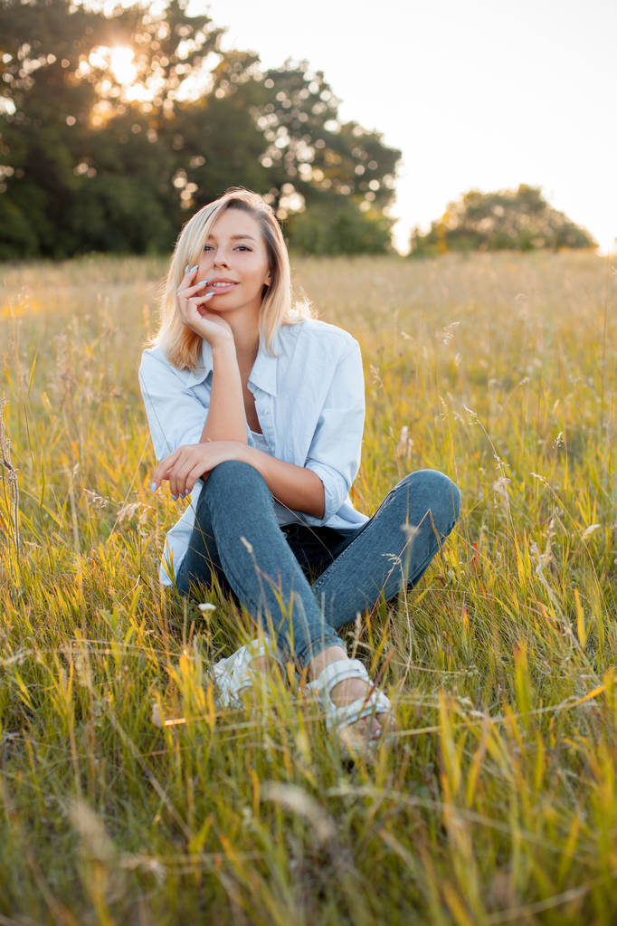 Jovem mulher sentada no campo verde sob a luz solar
 - Foto, Imagem