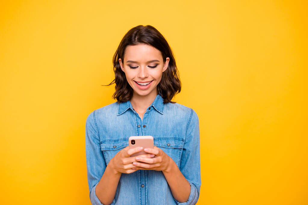 Portrét pozitivní veselá krásná dáma použít její mobilní telefon číst zprávy formulář sociální sítě účet post informace oblečení džíny košile izolované přes žlutou barvu pozadí - Fotografie, Obrázek