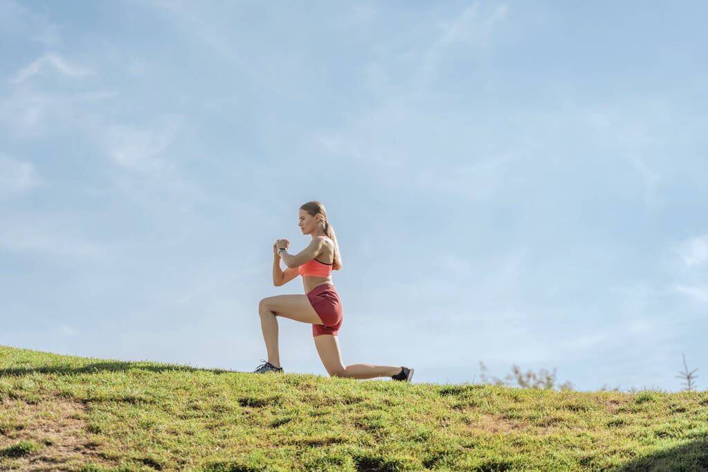 Athletic lady doing long step exercise on hill - 写真・画像