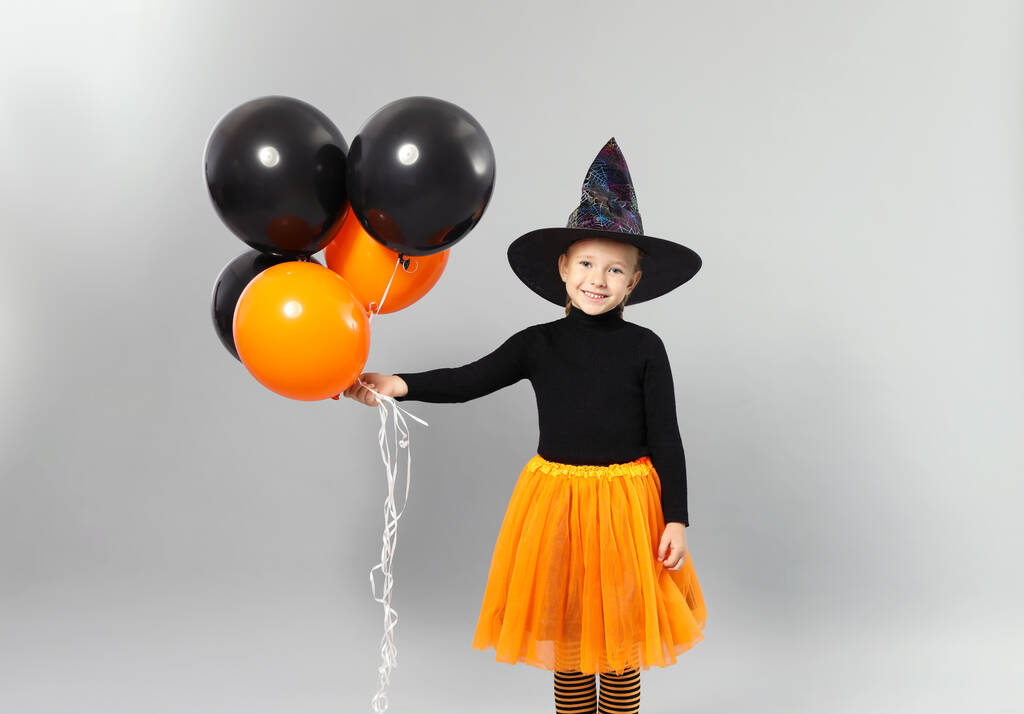 Balonlu şirin küçük kız gri arka planda Cadılar Bayramı kostümü giyiyor. - Fotoğraf, Görsel