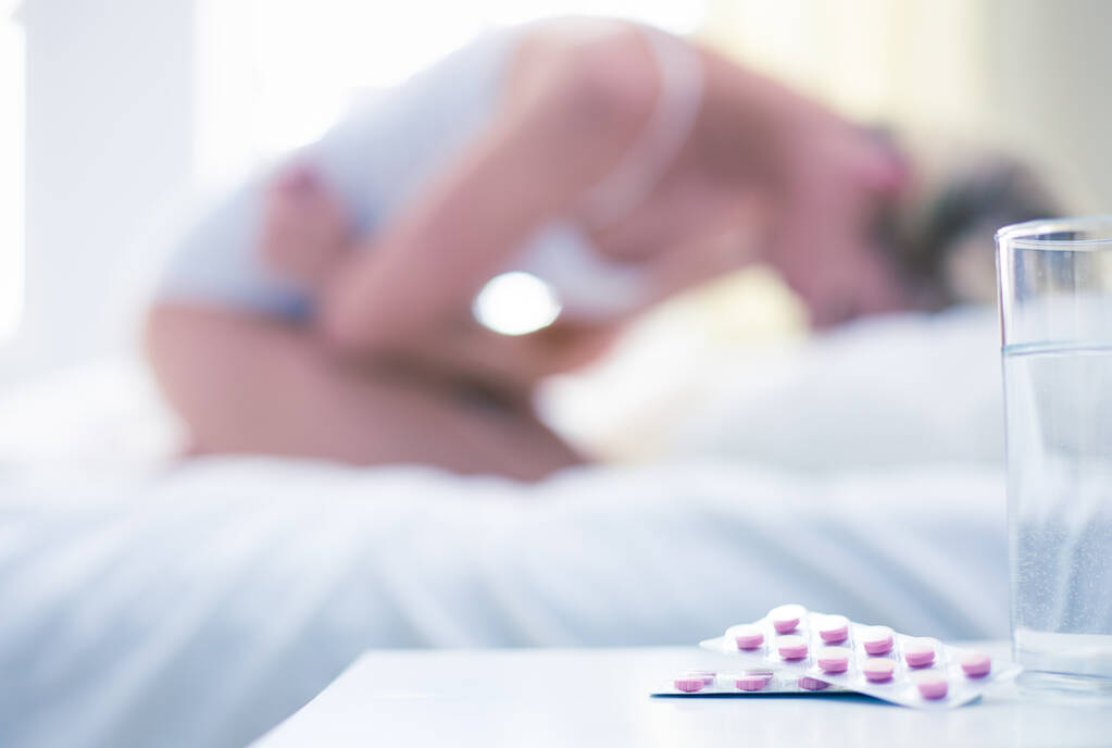 Jovem mulher bonita com pílulas deitadas na cama no quarto
 - Foto, Imagem