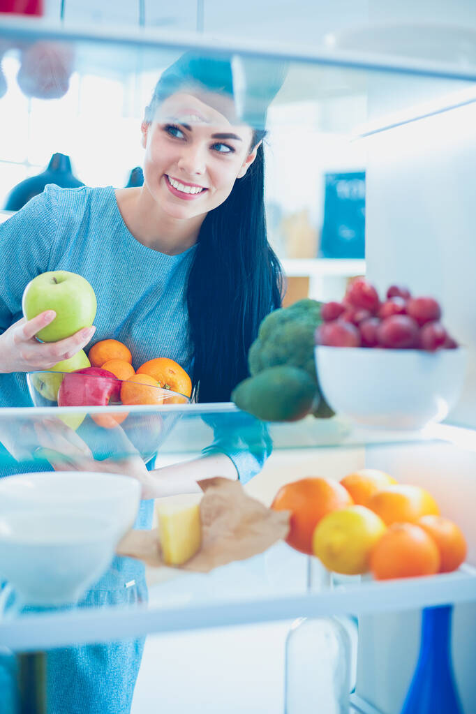 Mosolygó nő vesz egy friss gyümölcsöt ki a hűtőből, egészséges étel koncepció - Fotó, kép