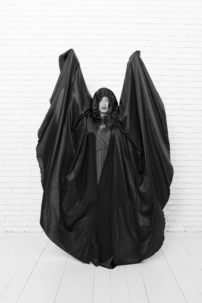 Смотри, это мой костюм на Хэллоуин. Чувственная женщина, одетая как Хеллоуинская ведьма на белой кирпичной стене. Сексуальная девушка в черной тоге на Хэллоуин. Подготовка и празднование Хэллоуина
 - Фото, изображение