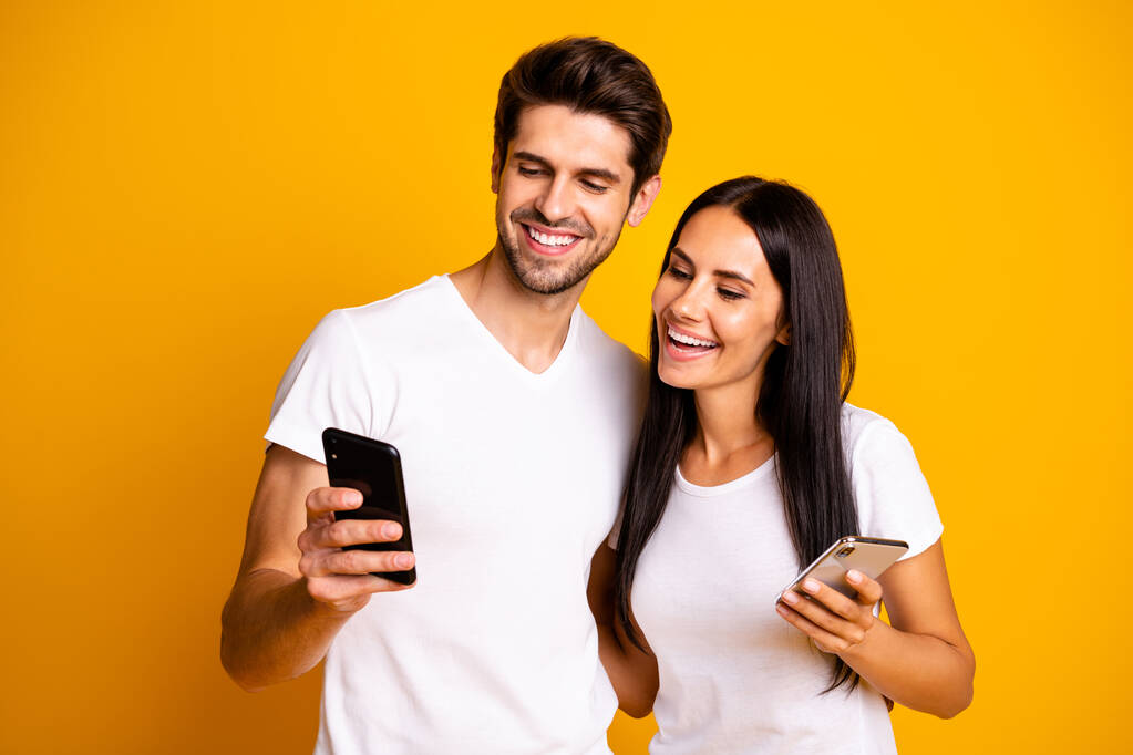 Fénykép két ember gazdaság telefonok néz vicces humoros videó viselet alkalmi ruhák elszigetelt sárga háttér - Fotó, kép