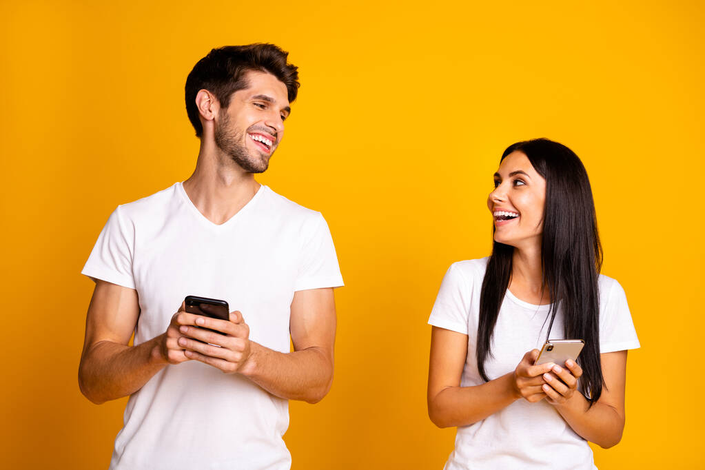 Foto von zwei Personen, die Telefone in der Hand halten und Feednews überprüfen, lachen über gute Witze tragen lässige Kleidung isoliert gelben Farbhintergrund - Foto, Bild
