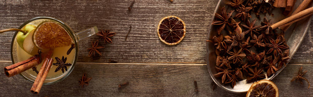 Draufsicht auf warmen Birnenglühwein mit Gewürzen und getrockneten Zitrusfrüchten auf Holztisch, Panoramaaufnahme - Foto, Bild