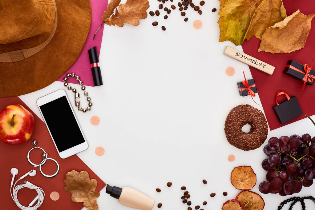 смартфон, капелюх, сухе листя, свіжі та сухі яблука, виноград, пончик, косметика, кавові зерна та дерев'яний блок з листопадовим написом ізольовані на білому
 - Фото, зображення