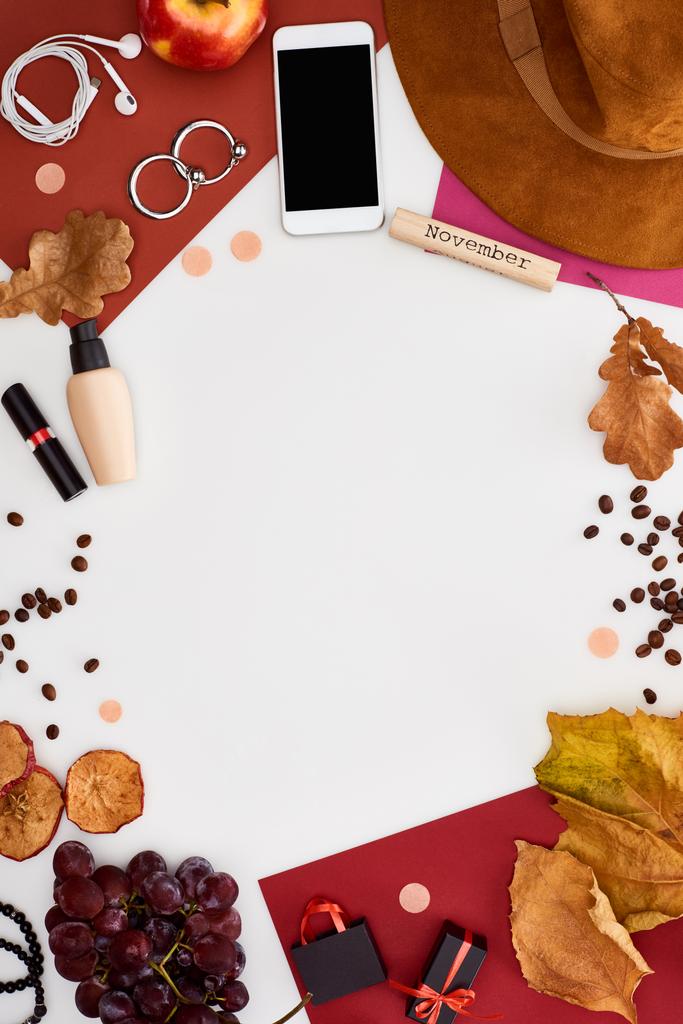 smartfon, kapelusz, suche liście, świeże i suche jabłka, winogrona, pączki, kosmetyki, ziarna kawy i drewniany blok z napisem listopadowym na białym - Zdjęcie, obraz