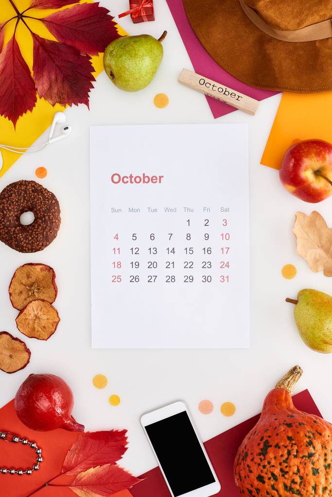 10月のカレンダーページ、帽子、スマートフォン、果物、カボチャ、乾燥した葉、多色の紙、白で隔離された10月の碑文を持つ木製のブロック - 写真・画像