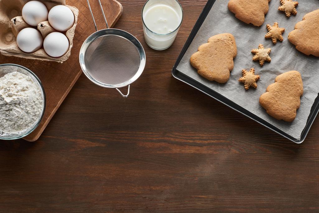 vue du dessus des biscuits de Noël sur le plateau du four près des ingrédients sur la table en bois
 - Photo, image