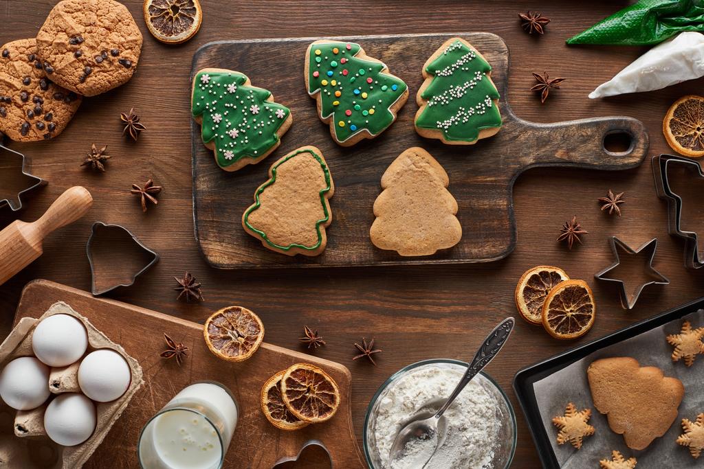 vista superior de biscoitos de árvore de Natal perto de ingredientes em mesa de madeira
 - Foto, Imagem