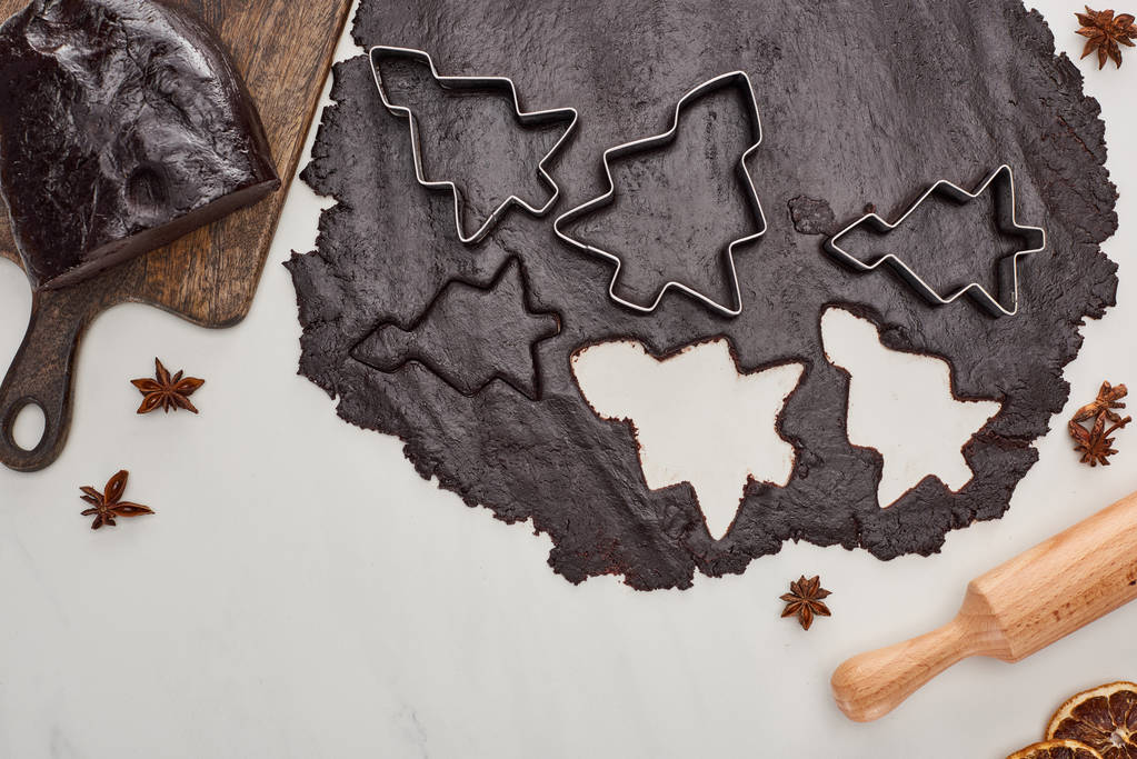bovenaanzicht van rauw deeg voor chocolade Kerstkoekjes op witte achtergrond bij anijs en deegroller - Foto, afbeelding