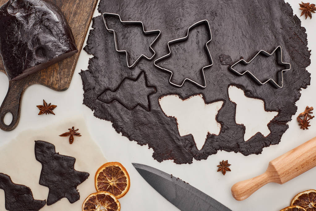 πάνω όψη ακατέργαστης ζύμης για μπισκότα σοκολάτας Χριστουγεννιάτικα σε λευκό φόντο κοντά σε γλυκάνισο, μαχαίρι και πλάστη - Φωτογραφία, εικόνα