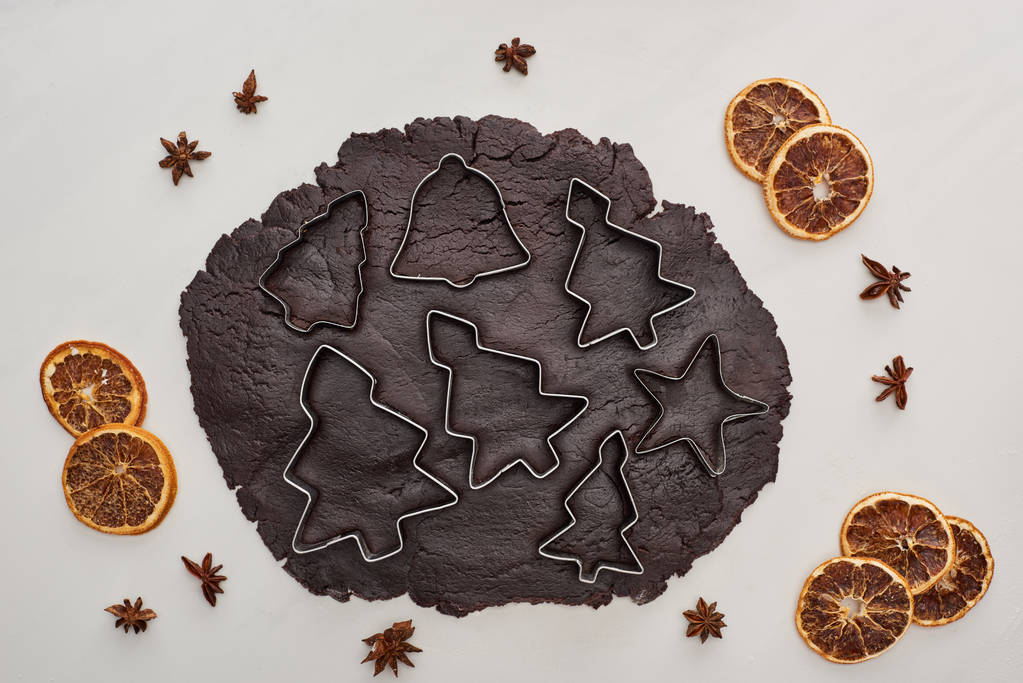 vista superior da massa crua para biscoitos de Natal de chocolate com moldes de massa no fundo branco perto de anis e citrinos secos
 - Foto, Imagem