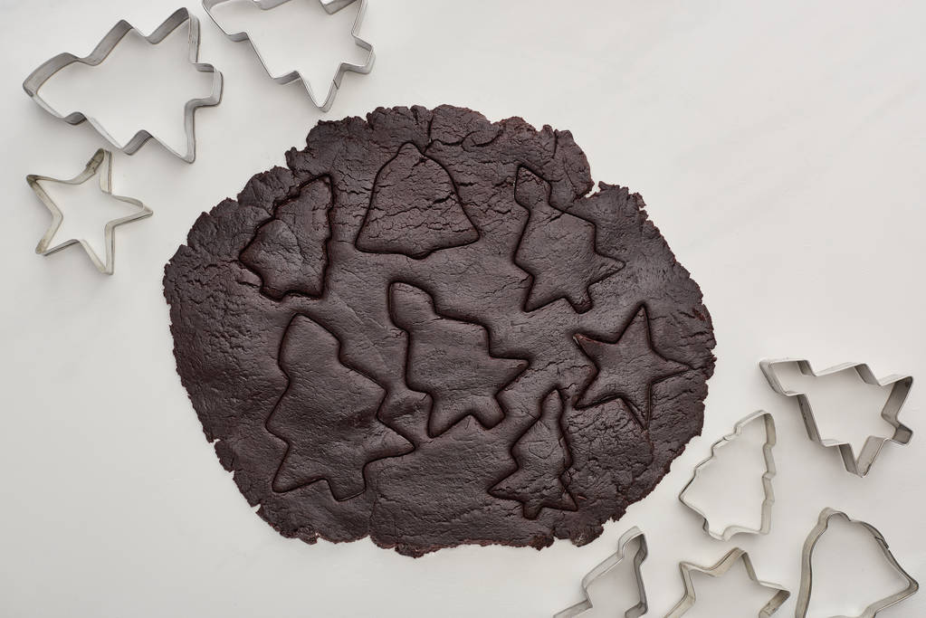 vista superior de la masa cruda para galletas de Navidad de chocolate sobre fondo blanco cerca de moldes de masa
 - Foto, Imagen