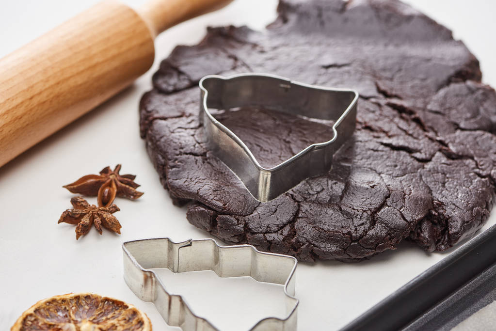 pâte crue pour biscuits de Noël au chocolat près de rouleau à pâtisserie et moules à pâte sur fond blanc
 - Photo, image