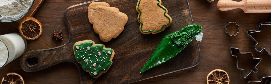 vista superior de biscoitos de Natal envidraçados com saco de pastelaria na mesa de madeira, tiro panorâmico
 - Foto, Imagem