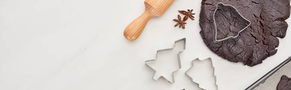 vista superior de la masa cruda para galletas de Navidad de chocolate cerca de rodillo y moldes de masa sobre fondo blanco, plano panorámico
 - Foto, Imagen