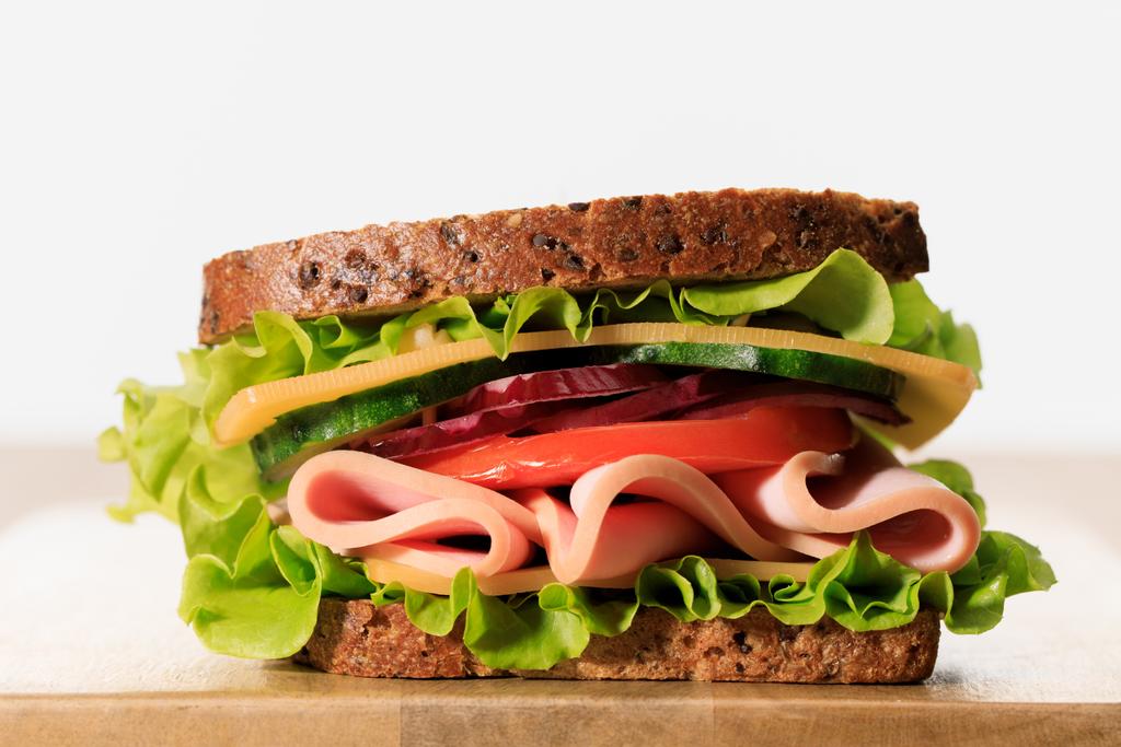 verse sandwich met sla, ham, kaas, spek en tomaat op houten snijplank geïsoleerd op wit - Foto, afbeelding