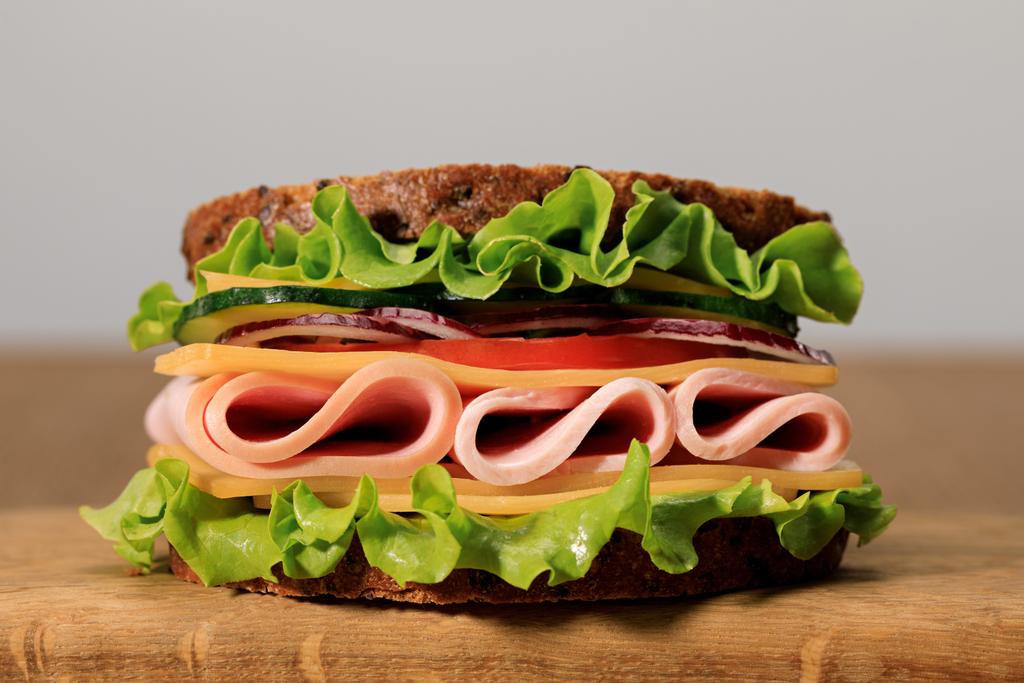 sándwich fresco con lechuga, jamón, queso, tocino y tomate sobre tabla de cortar de madera aislada en gris
 - Foto, Imagen