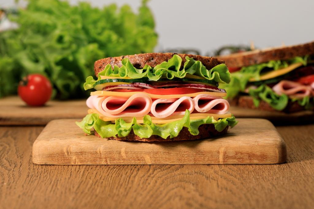 fresh sandwich with lettuce, ham, cheese, bacon and tomato on wooden cutting board isolated on grey - Photo, Image