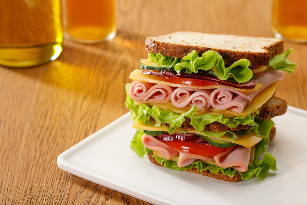 foco seletivo de sanduíche fresco com alface, presunto, queijo, bacon e tomate perto de garrafas de cerveja na mesa de madeira
 - Foto, Imagem