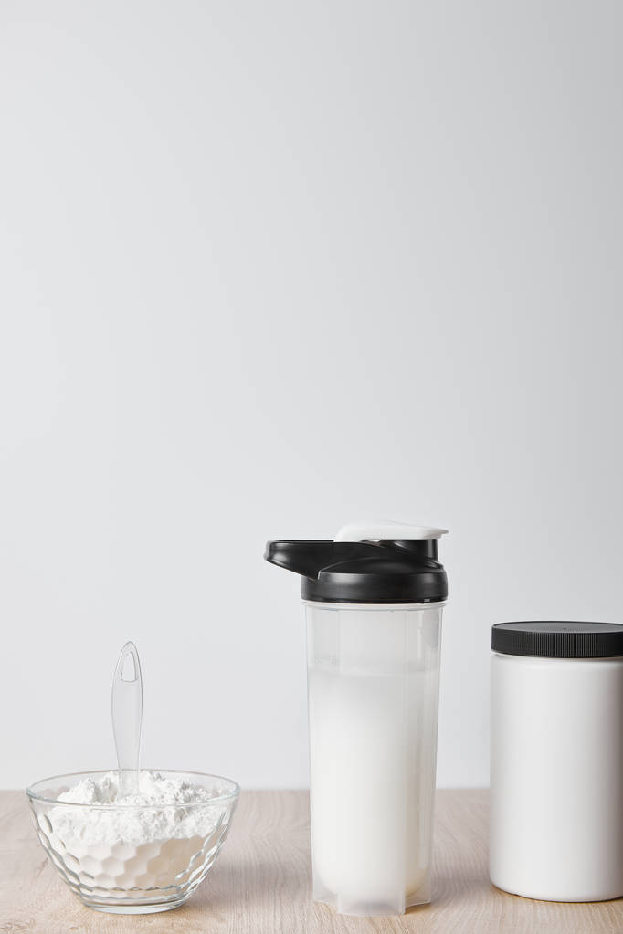 білковий струс у спортивній пляшці поблизу банки та скляної миски з білковим струмом ізольовано на сірому
 - Фото, зображення