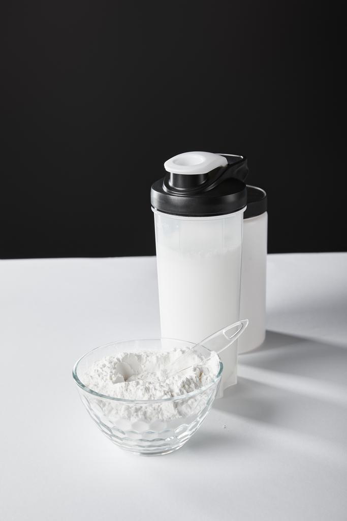 szklana miska z proszkiem białkowym w pobliżu butelek sportowych i słoik na czarno  - Zdjęcie, obraz