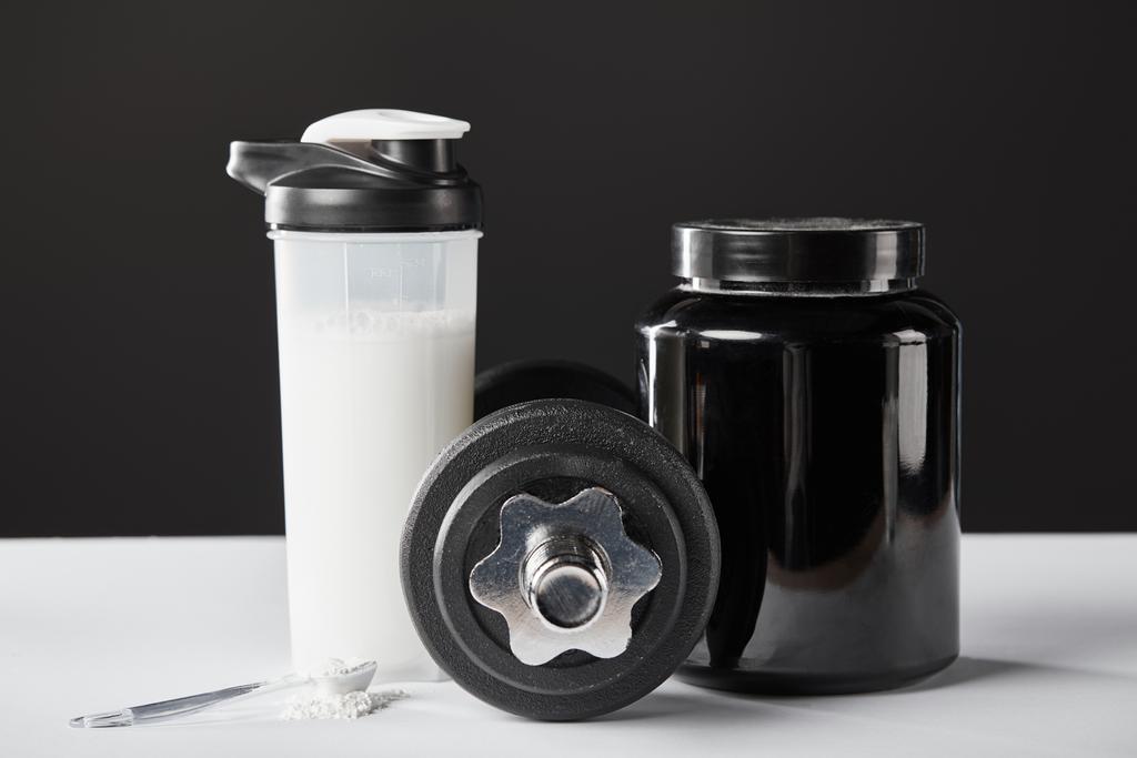 cuillère près haltère et bouteille de sport avec shake de protéines sur noir
  - Photo, image