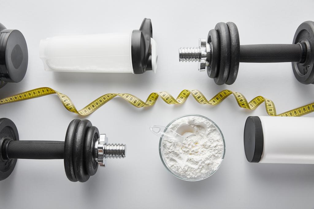 vista superior de halteres pesados perto de garrafa de esportes e fita métrica em branco
  - Foto, Imagem