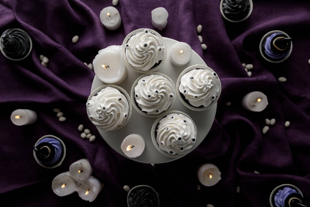 vista superior de deliciosos cupcakes de Halloween cerca de velas encendidas en tela púrpura
 - Foto, imagen