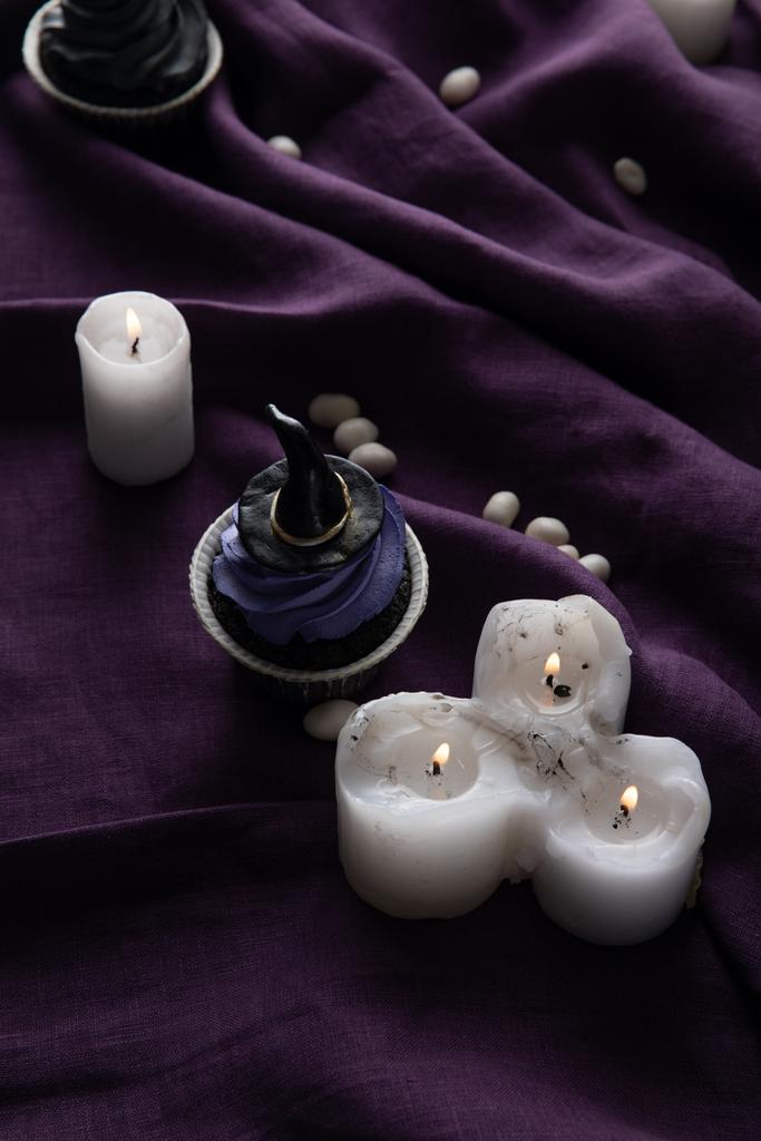 heerlijke Halloween cupcakes in de buurt van brandende kaarsen op paarse doek - Foto, afbeelding