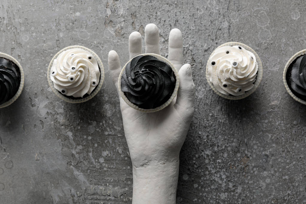 top view of delicious Halloween cupcake in decorative hand on concrete grey surface - 写真・画像
