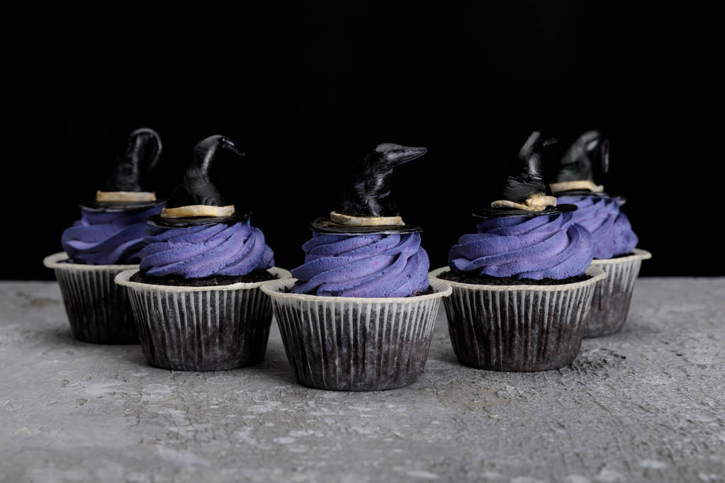 Halloween cupcakes s modrým krémem a dekorativní čarodějnické klobouky na betonové šedé povrchu izolované na černé - Fotografie, Obrázek