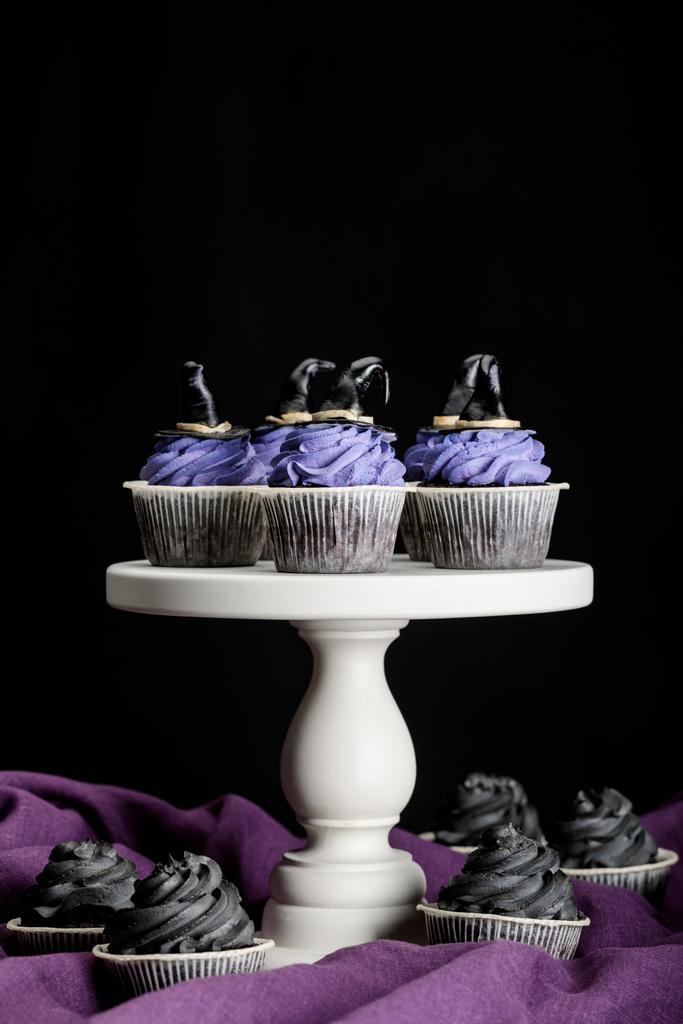 sabrosos cupcakes de Halloween en soporte blanco en paño púrpura aislado en negro
 - Foto, imagen