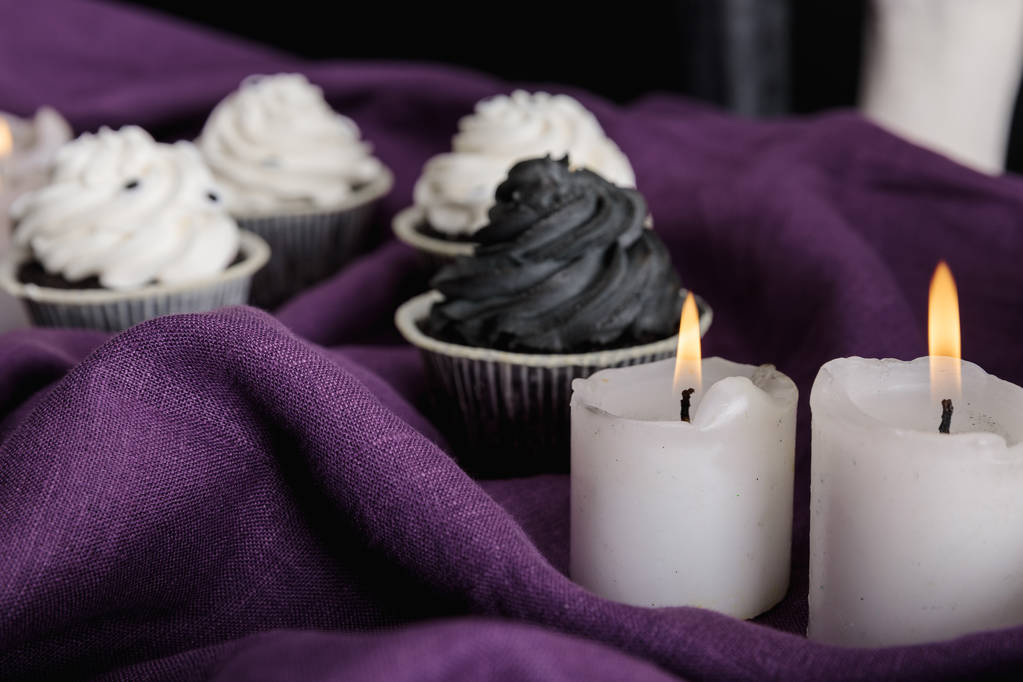 selectieve focus van lekkere Halloween cupcakes en brandende kaarsen op paarse doek - Foto, afbeelding