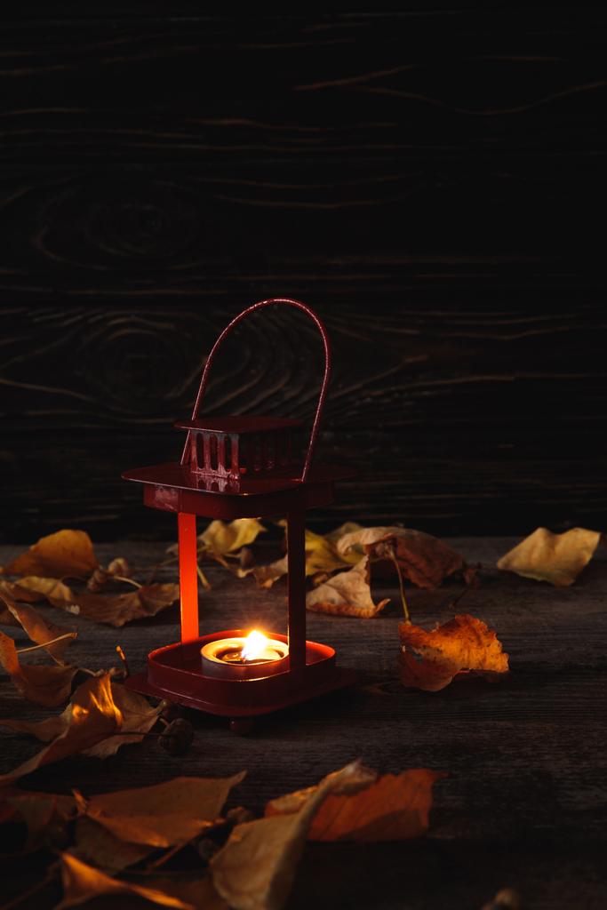 ξηρά φθινοπωρινά φύλλα και αναμμένο κερί σε ξύλινο ρουστίκ τραπέζι σε μαύρο φόντο - Φωτογραφία, εικόνα