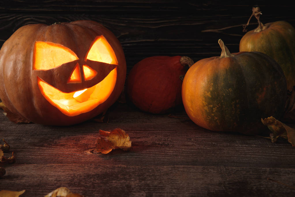 abóbora assustadora esculpida Halloween, folhas de outono e vela ardente na mesa rústica de madeira
 - Foto, Imagem