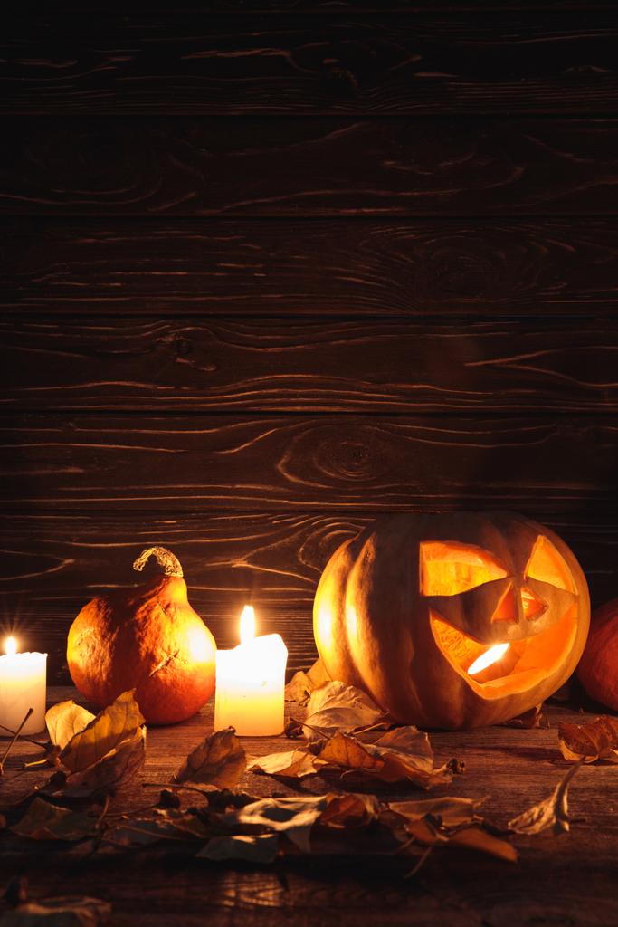 carved spooky Halloween pumpkin, autumnal leaves and burning candles on wooden rustic table - 写真・画像