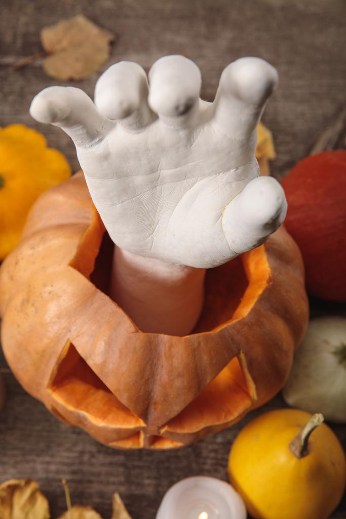 vrchní pohled na dekorativní ruku v vyřezávané Halloween dýně na dřevěném rustikálním stole - Fotografie, Obrázek
