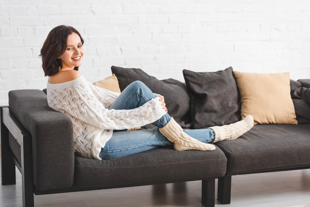 attraente donna bruna seduta sul divano con cuscini in accogliente soggiorno
  - Foto, immagini