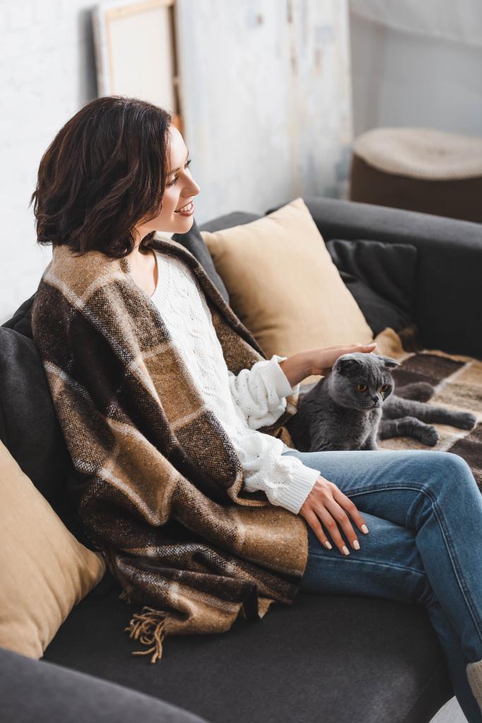 attraktive Frau in Decke sitzt auf Sofa mit Katze   - Foto, Bild