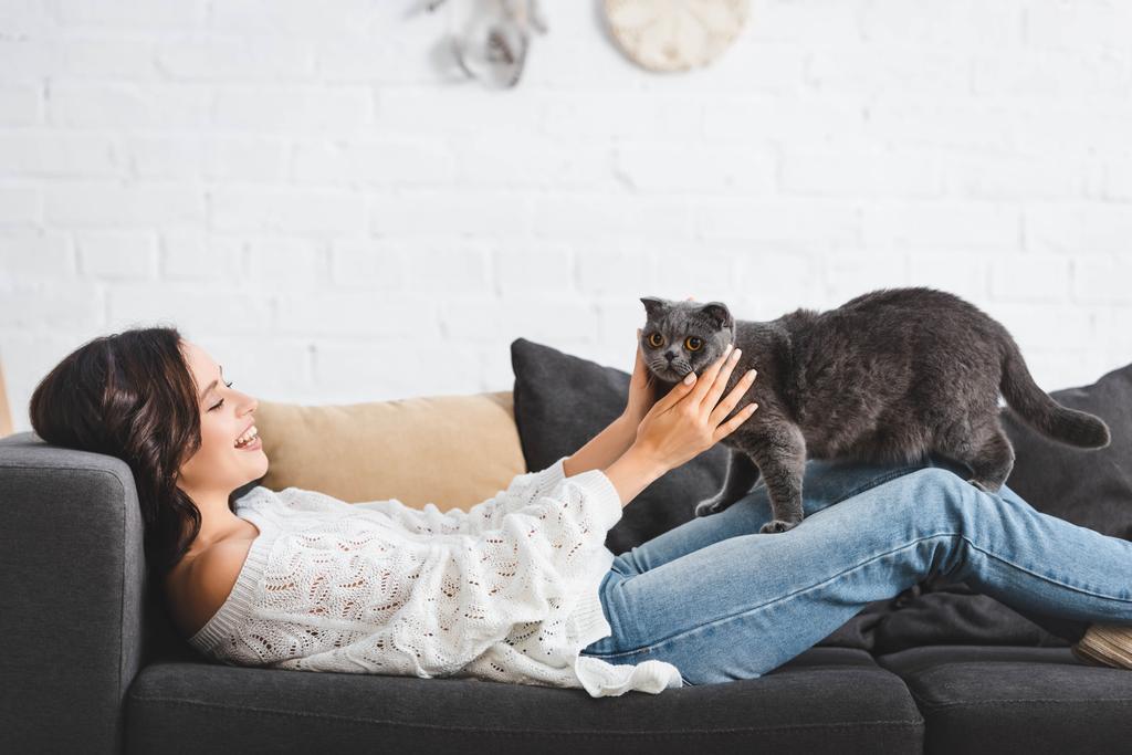 brunette woman lying on sofa with scottish fold cat in cozy living room - Photo, Image