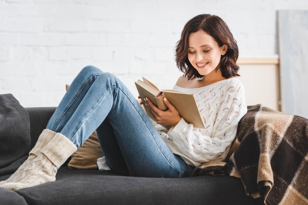 Lächelndes Mädchen liest Buch zu Hause auf dem Sofa - Foto, Bild